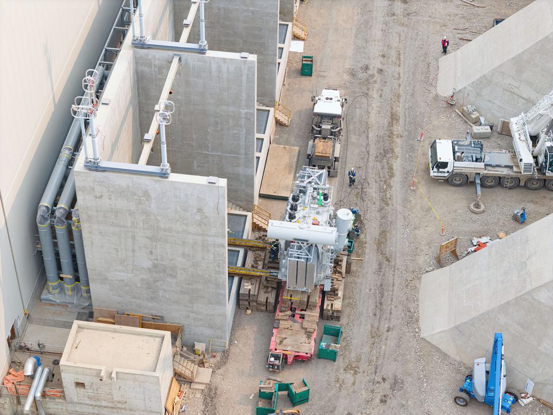 The first assembled transformer is moved onto the transformer foundation by a specialized heavy lift crew. Transformers receive the electrical current generated in the powerhouse and transfer it into the transmission system.